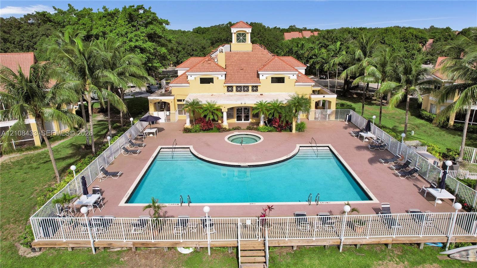 2300 NW 33rd Street, #911, Oakland Park, FL 33309 Mediterranean-style clubhouse featuring a terra-cotta tile roof and a central observation tower, accompanied by a fenced outdoor pool and spa surrounded by a paved deck
