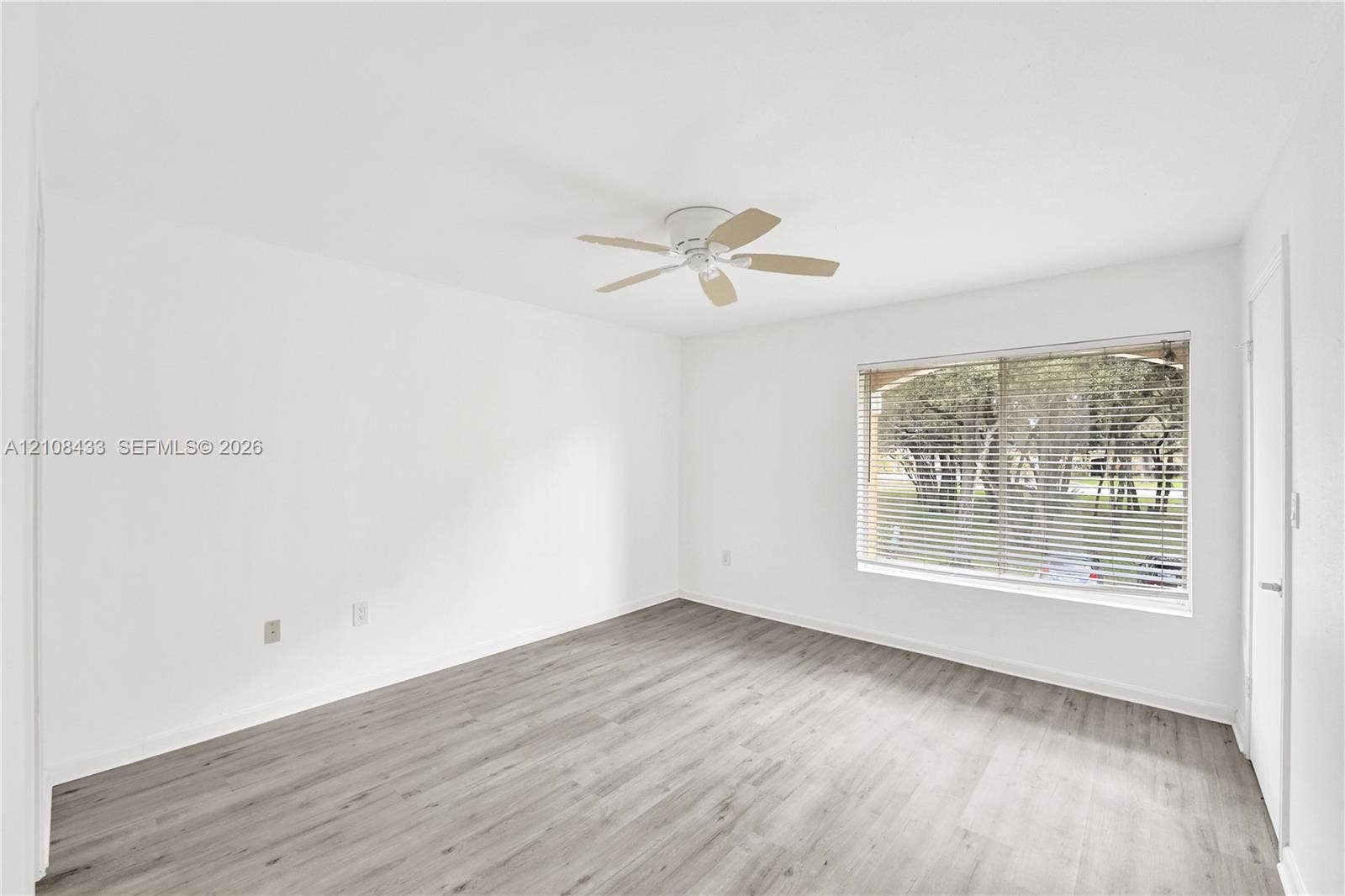 2300 NW 33rd Street, #911, Oakland Park, FL 33309 Neutral-toned walls, wood-finish flooring, ceiling-mounted fan, and a large window with horizontal blinds