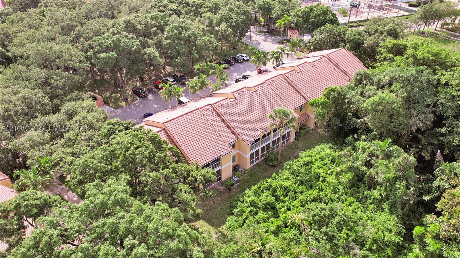 2300 NW 33rd Street, #911, Oakland Park, FL 33309 Multi-story residential building featuring a tile roof, light-toned exterior finish, screened balconies, and extensive surrounding tree canopy