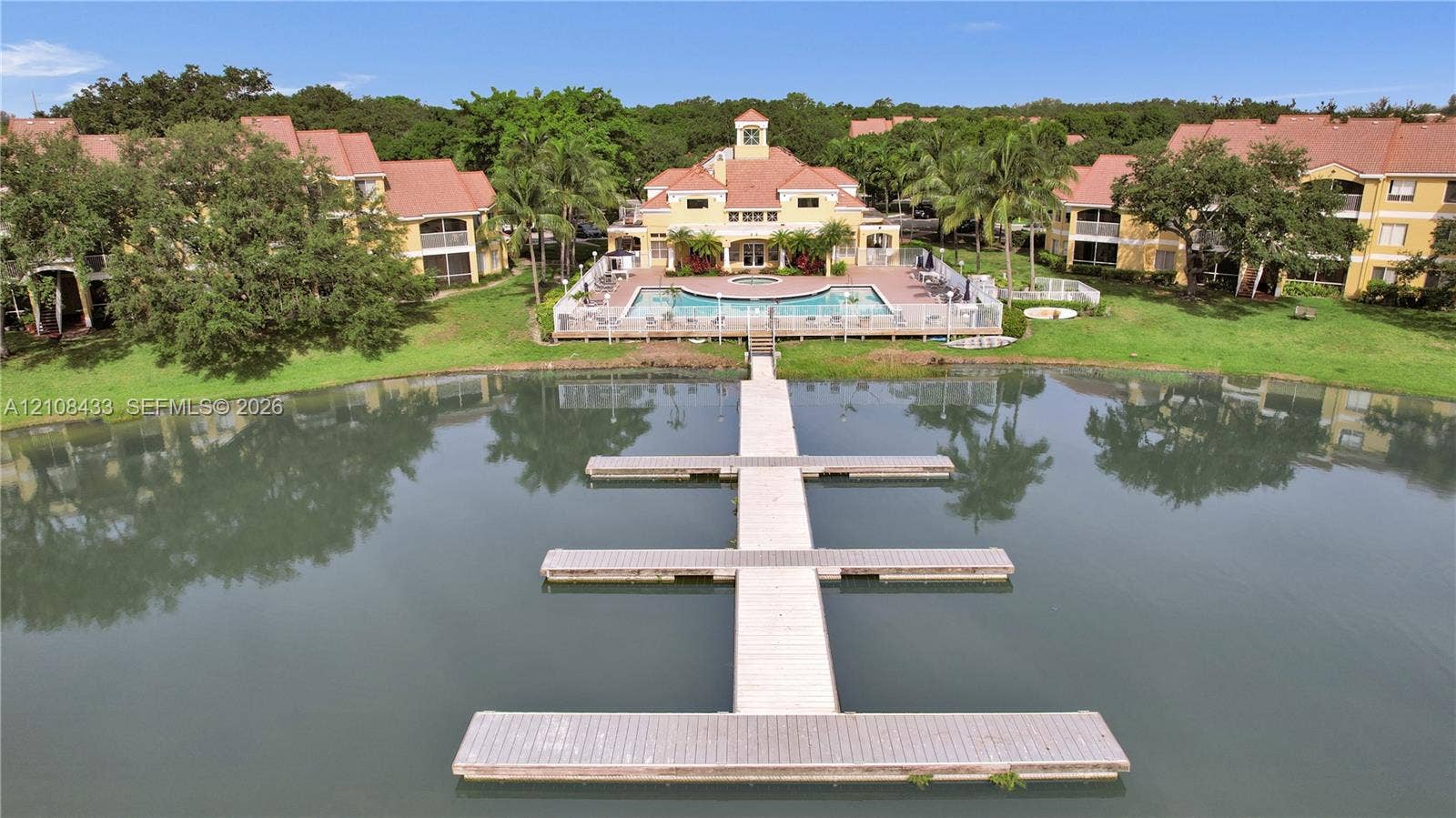 2300 NW 33rd Street, #911, Oakland Park, FL 33309 Multi-story residential complex featuring a swimming pool, tiled roof architecture, manicured green space, and a private dock extending into a lake