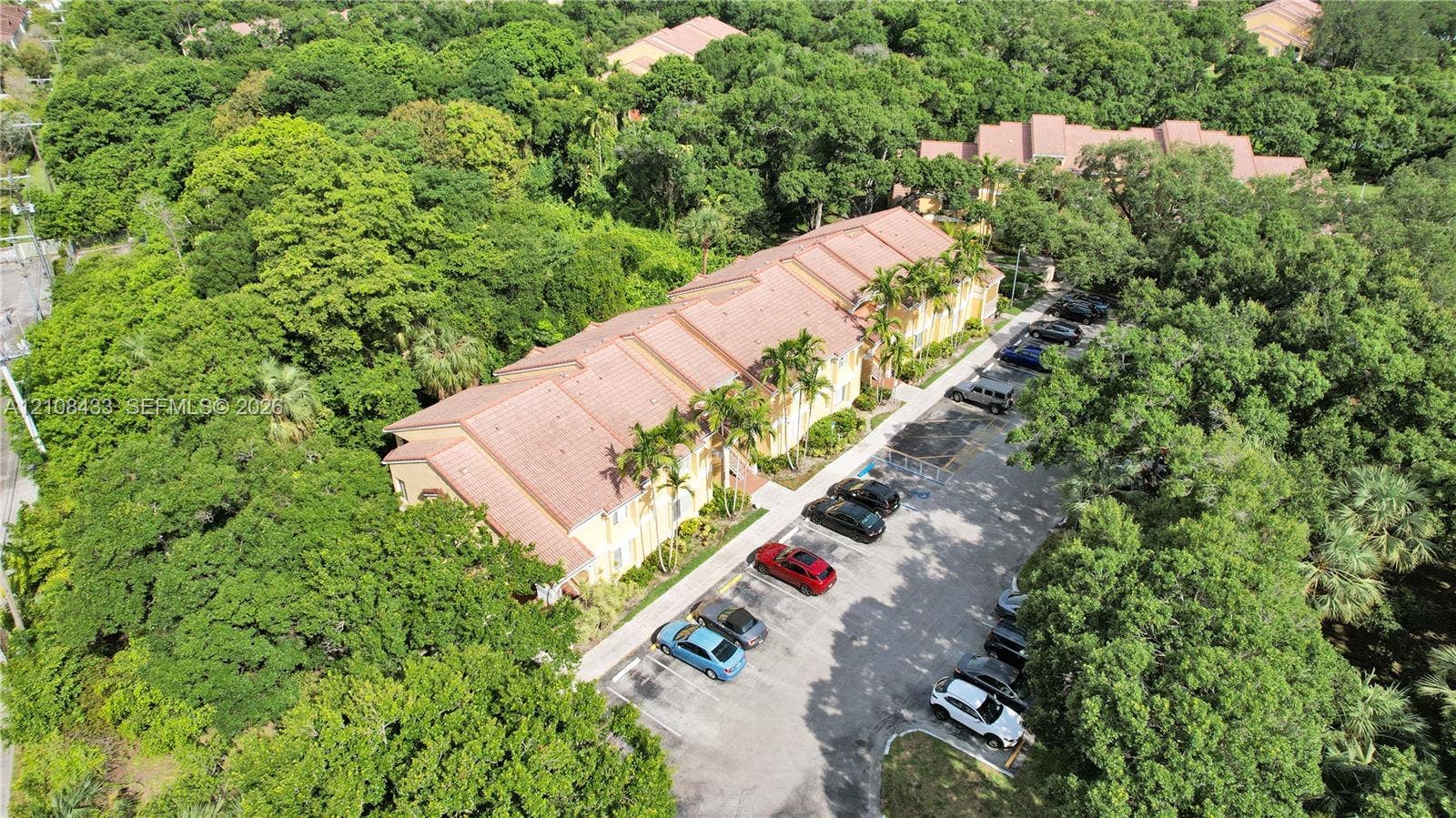 2300 NW 33rd Street, #911, Oakland Park, FL 33309 Multi-story building featuring a tile roof, exterior stucco siding, and designated asphalt surface parking, situated among mature trees and dense vegetation