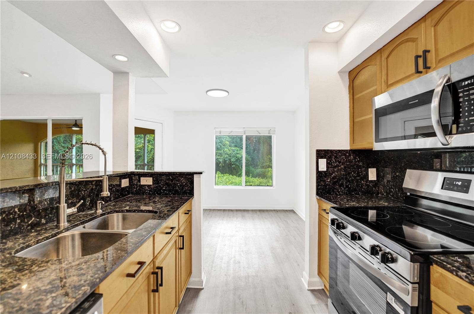 2300 NW 33rd Street, #911, Oakland Park, FL 33309 Kitchen featuring medium-tone wood cabinetry, dark stone countertops, stainless steel appliances, a dual-basin undermount sink, and wood-finish flooring