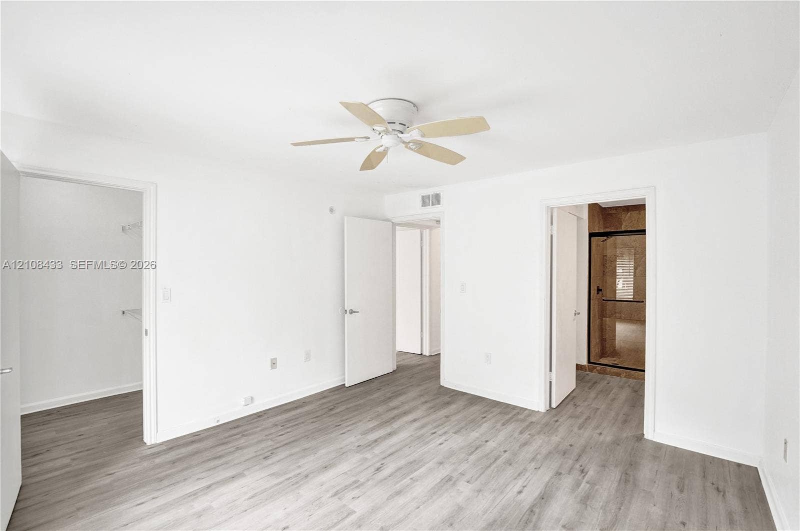 2300 NW 33rd Street, #911, Oakland Park, FL 33309 Neutral interior featuring wood-finish flooring, a ceiling fan with integrated lighting, and multiple interior doorways leading to a walk-in closet and a bathroom with a glass-enclosed shower