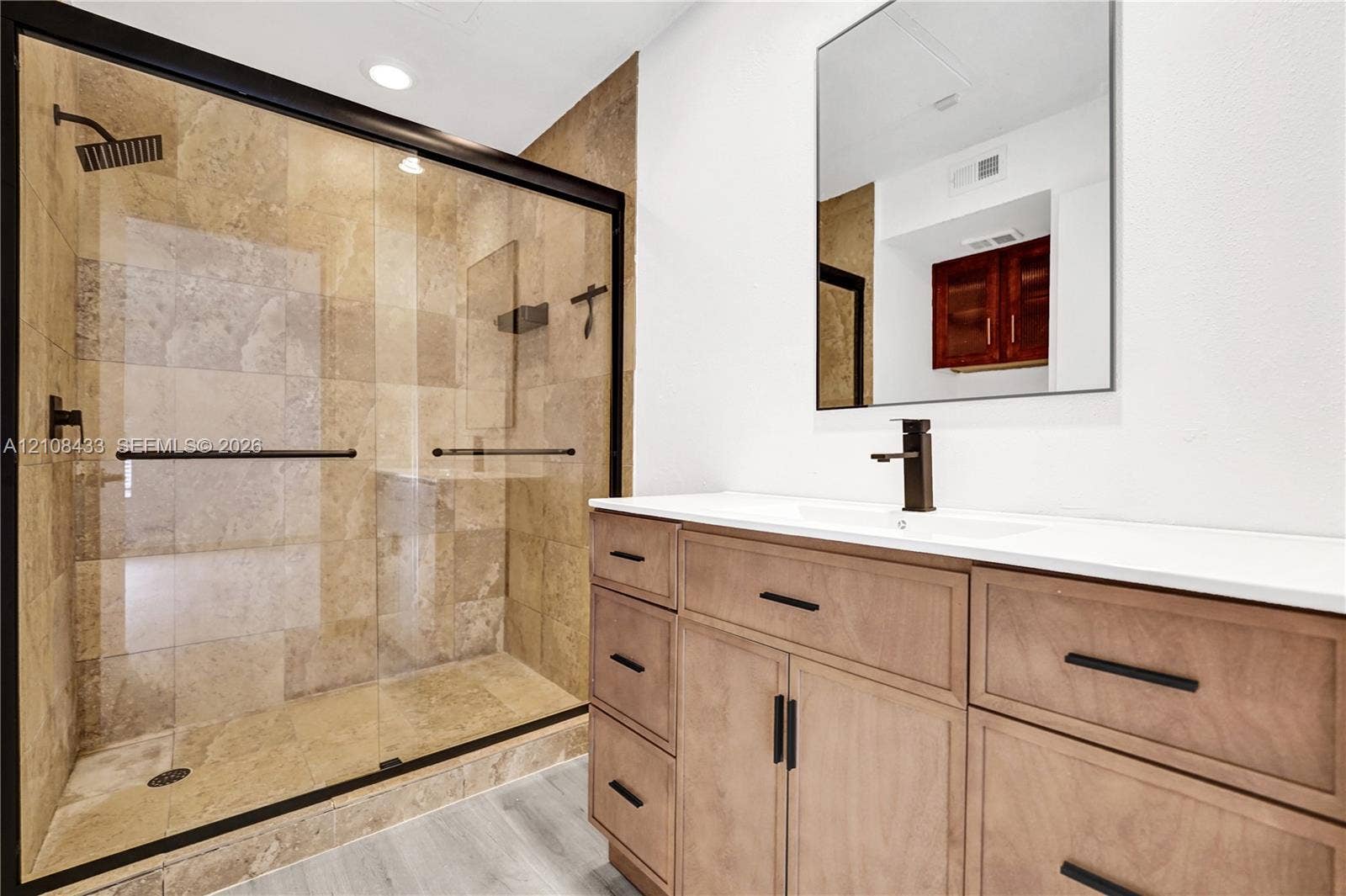 2300 NW 33rd Street, #911, Oakland Park, FL 33309 Walk-in shower with stone tile surround, frameless glass enclosure, and matte black fixtures