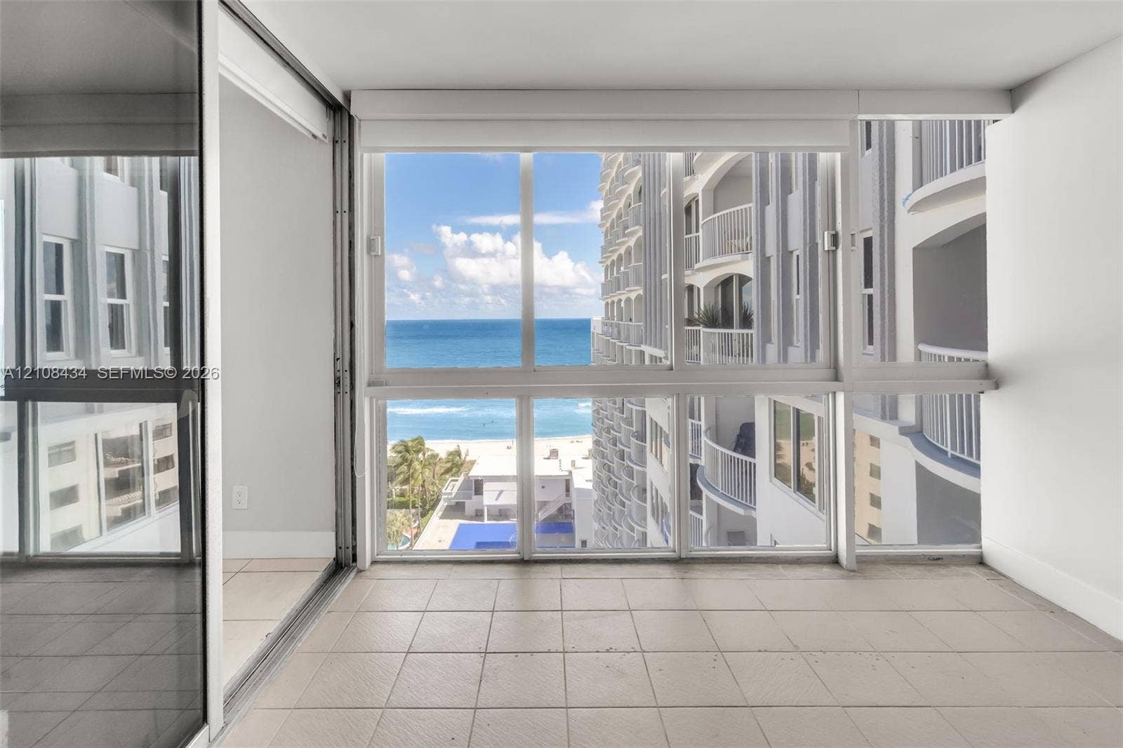 Miami Beach, FL 33140 Enclosed balcony featuring tile flooring, floor-to-ceiling windows, and sliding glass panel doors, showcasing ocean and coastline scenery
