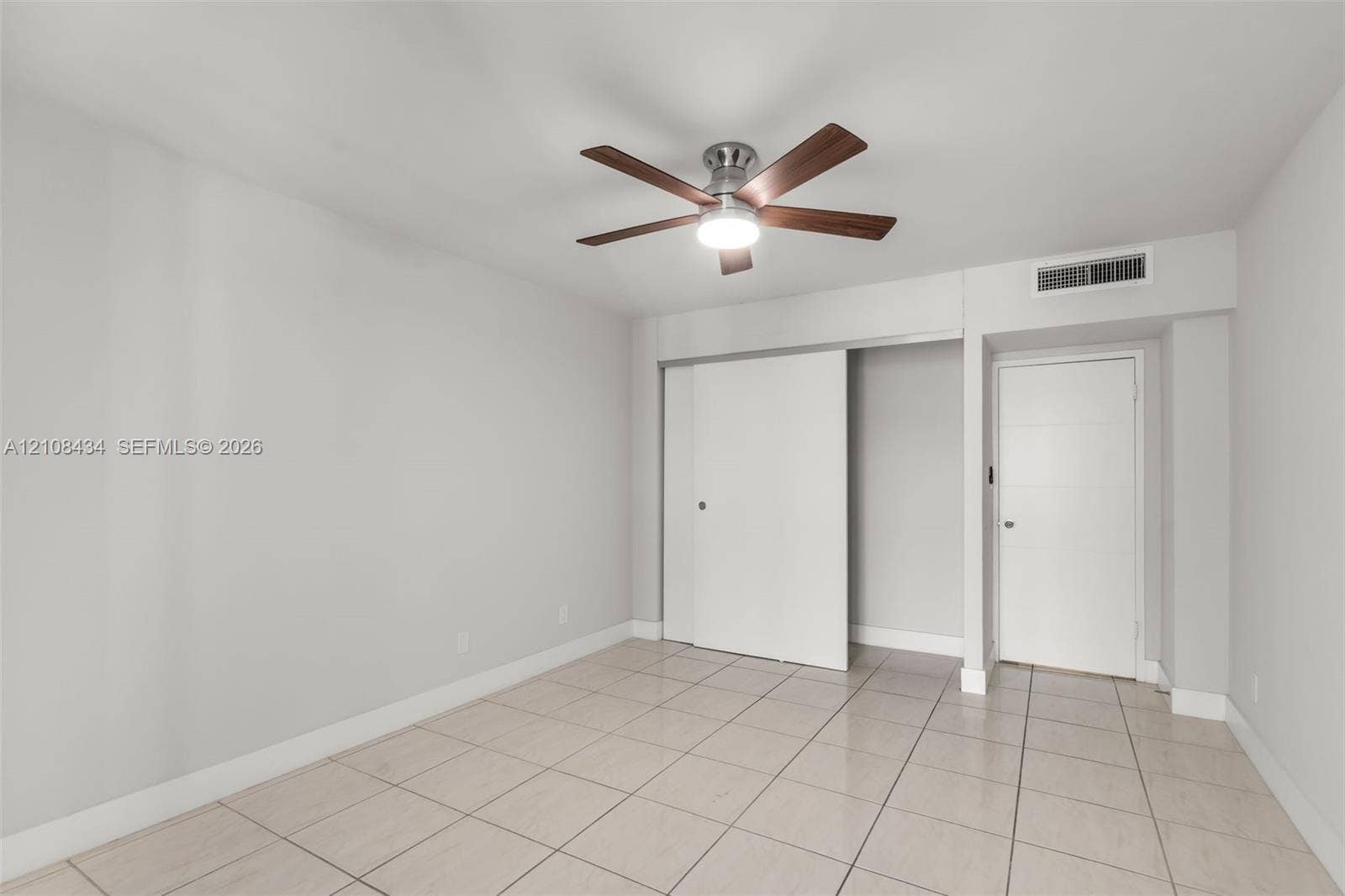 Miami Beach, FL 33140 Neutral-toned room featuring large-format tile flooring, a multi-blade ceiling fan with integrated lighting, a sliding-door closet, and a contemporary flat-panel door