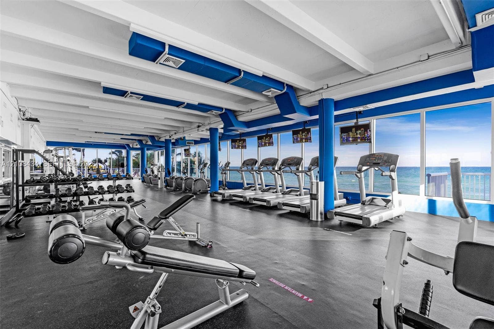 Miami Beach, FL 33140 Fitness center featuring floor-to-ceiling windows with ocean scenery, exposed white beam ceilings, industrial-style exposed ductwork, and resilient rubber flooring