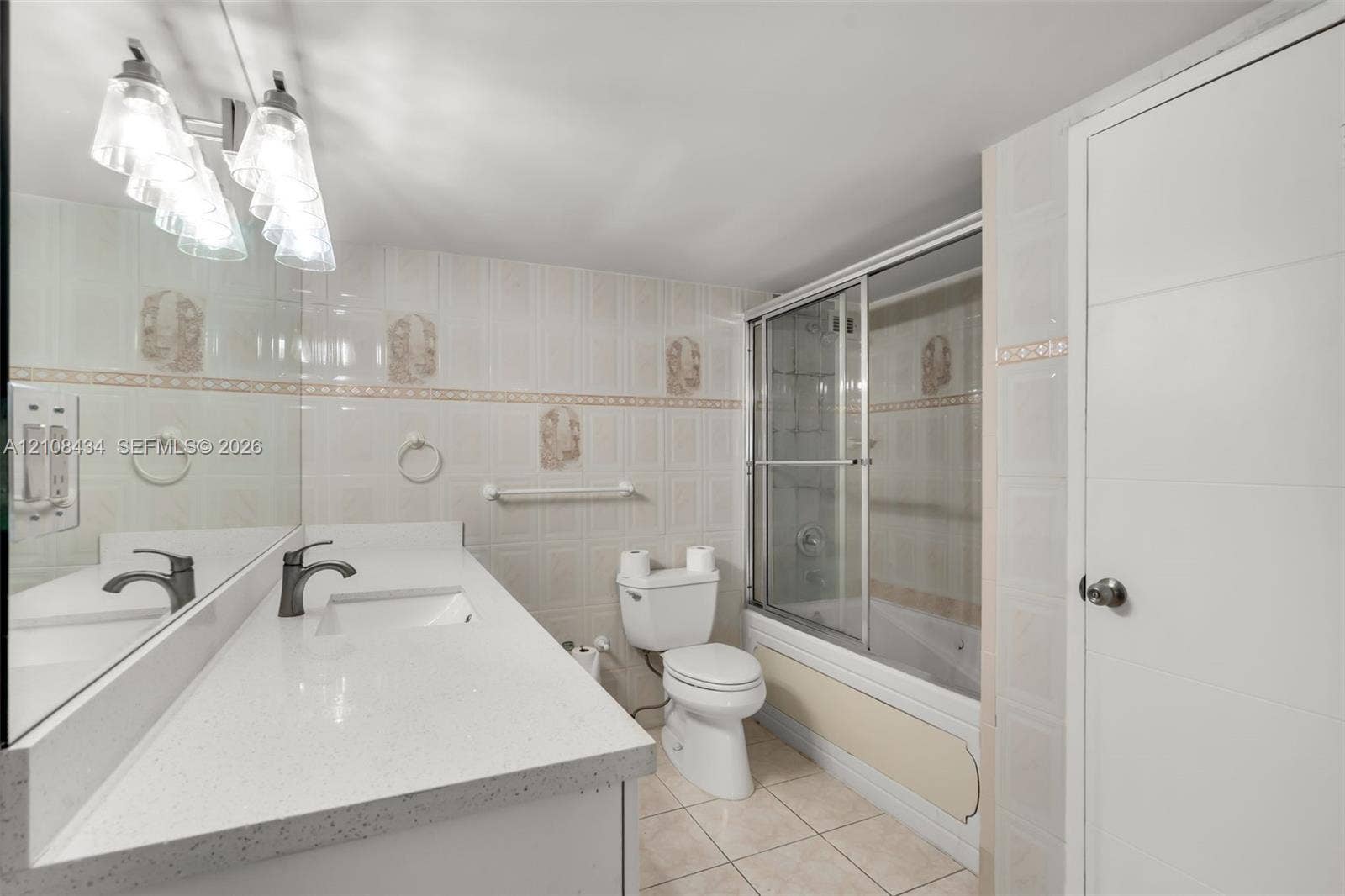 Miami Beach, FL 33140 Bathroom featuring a quartz-topped vanity with an integrated basin, ceramic tile flooring, full-width wall mirror, and a tub-shower combination enclosed by sliding glass doors