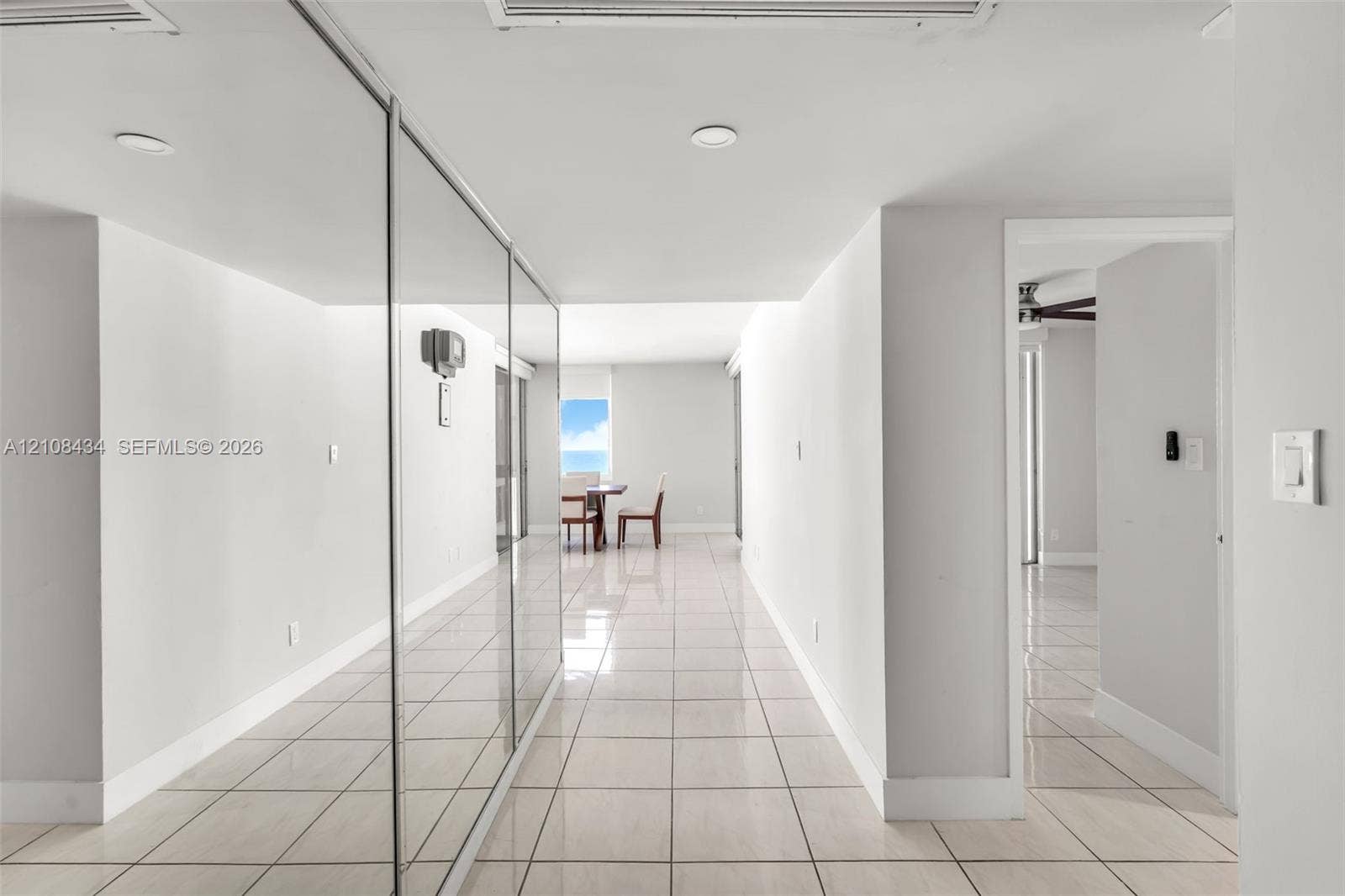 Miami Beach, FL 33140 Interior hallway featuring light-toned tile flooring, floor-to-ceiling mirrored wall panels, and recessed lighting