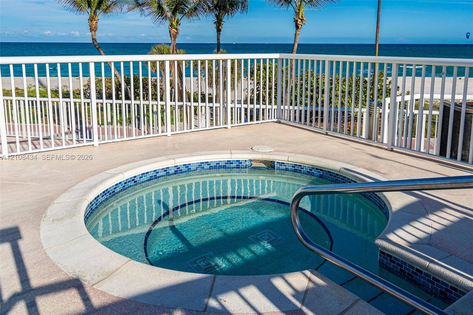 Miami Beach, FL 33140 Circular jetted spa with blue tile surround, concrete decking, metal safety railing, and ocean backdrop