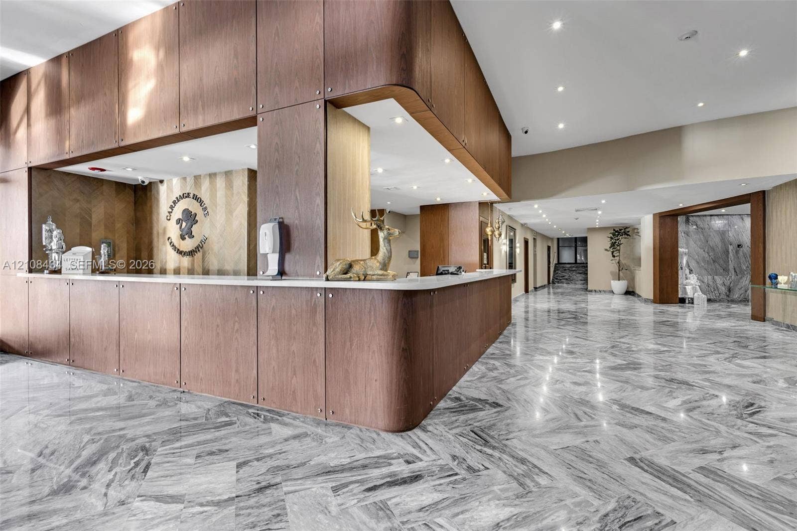 Miami Beach, FL 33140 Lobby area featuring polished natural stone flooring in a herringbone pattern, wood-panelled custom reception desk with a solid surface countertop, and recessed ceiling lighting