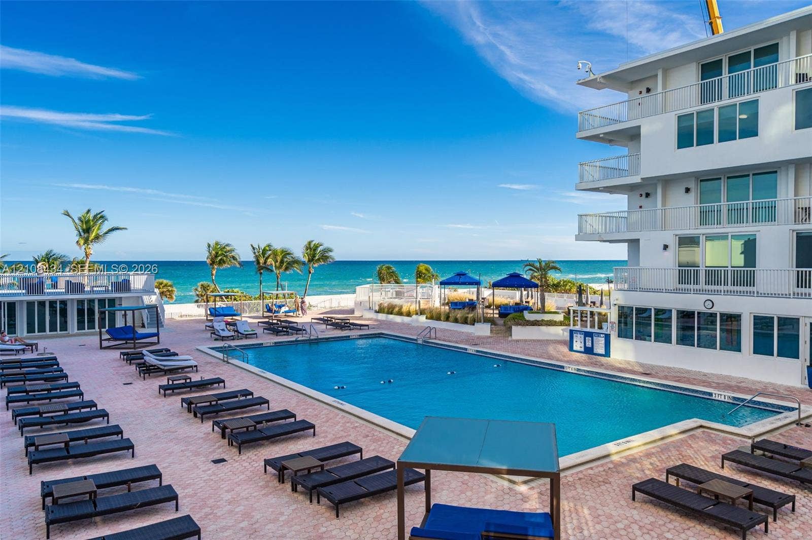 Miami Beach, FL 33140 In-ground rectangular swimming pool surrounded by a brick paver deck, multi-story building with private railed balconies, and direct oceanfront access