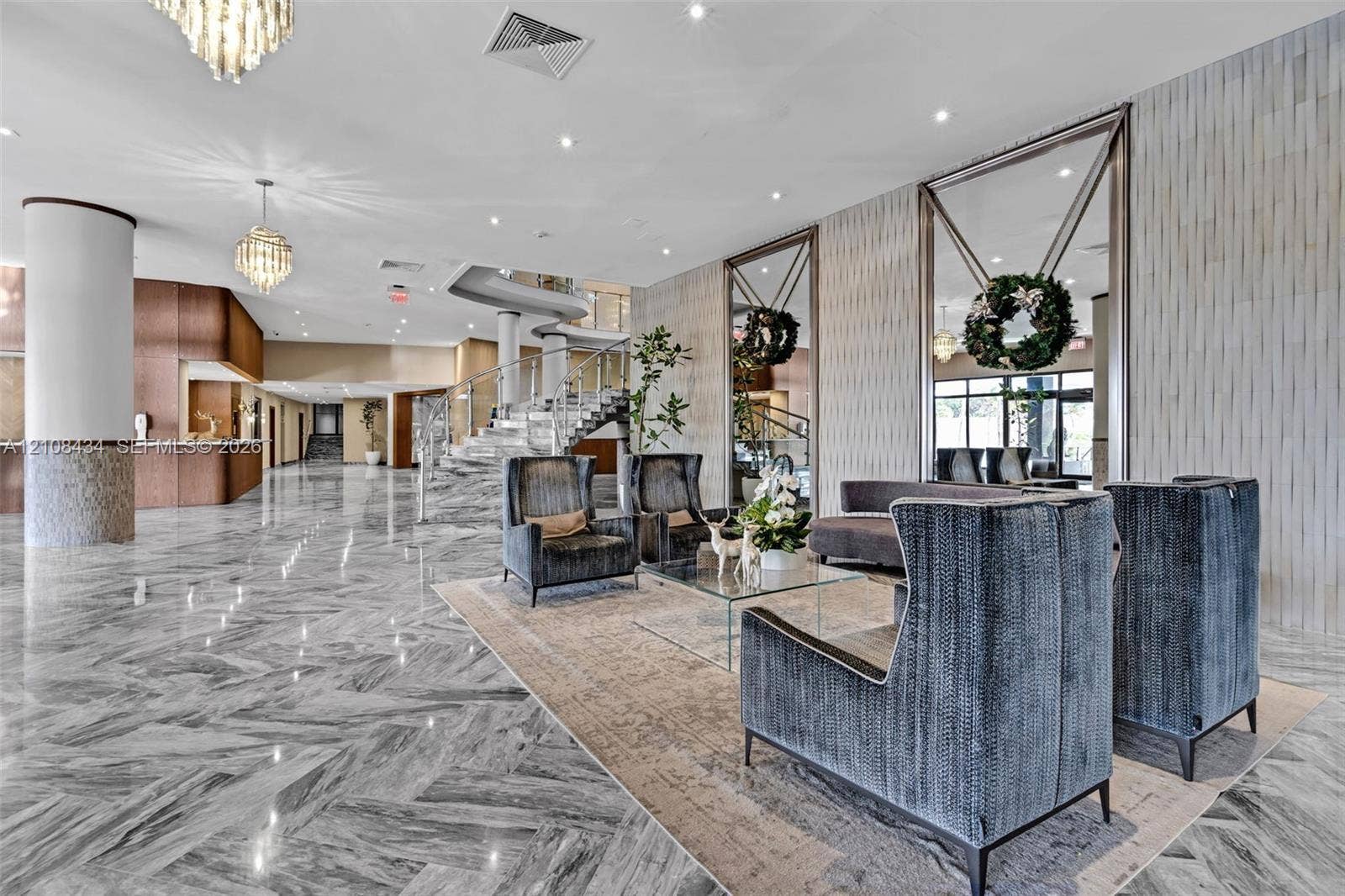 Miami Beach, FL 33140 Expansive lobby featuring polished stone flooring in a herringbone pattern, floor-to-ceiling decorative mirrors, recessed lighting, crystal chandeliers, and a sweeping staircase with a metal railing