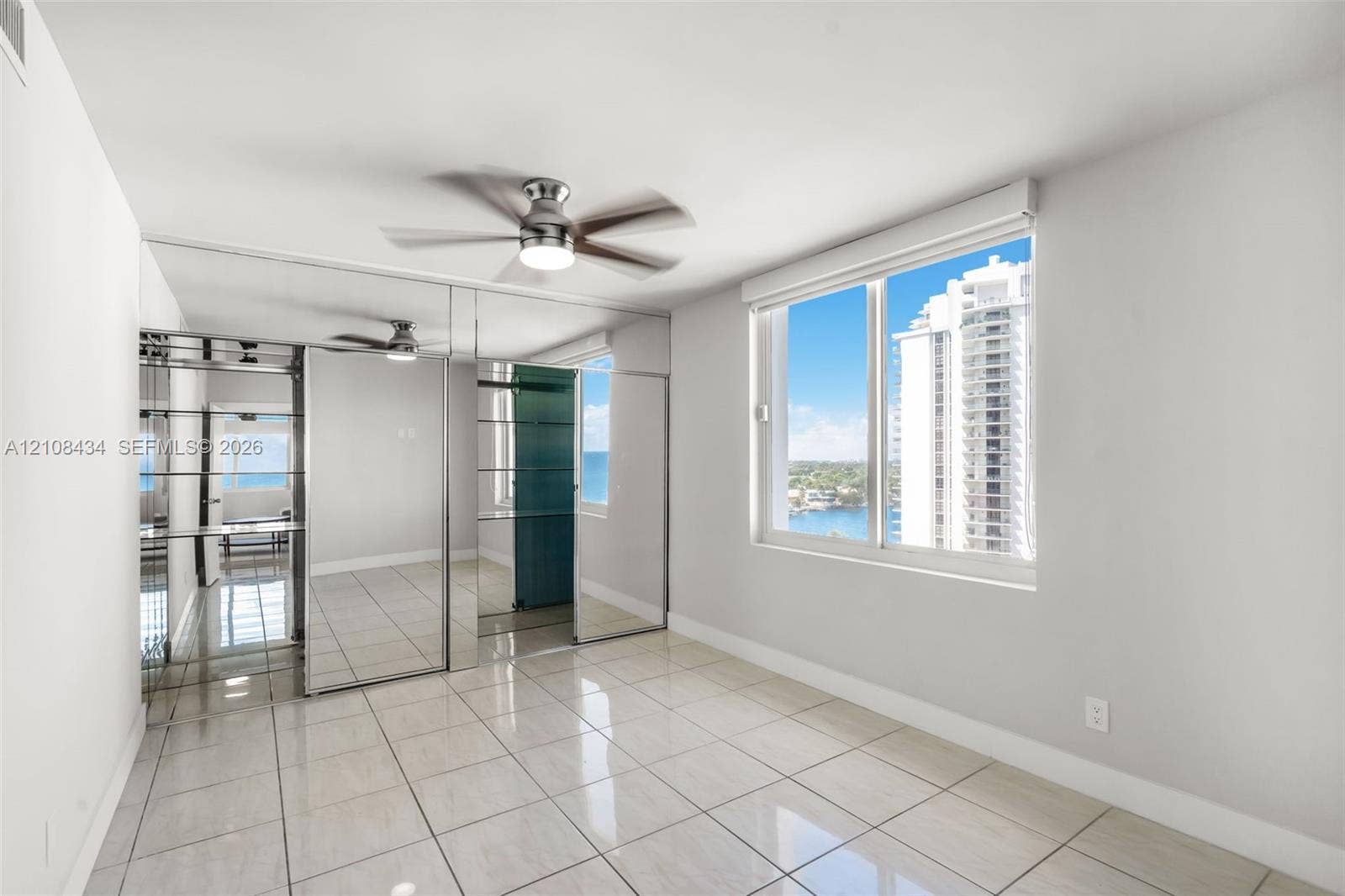 Miami Beach, FL 33140 Large format tile flooring, floor-to-ceiling mirrored closet doors, ceiling fan with integrated lighting, and expansive window with water and skyline exposure