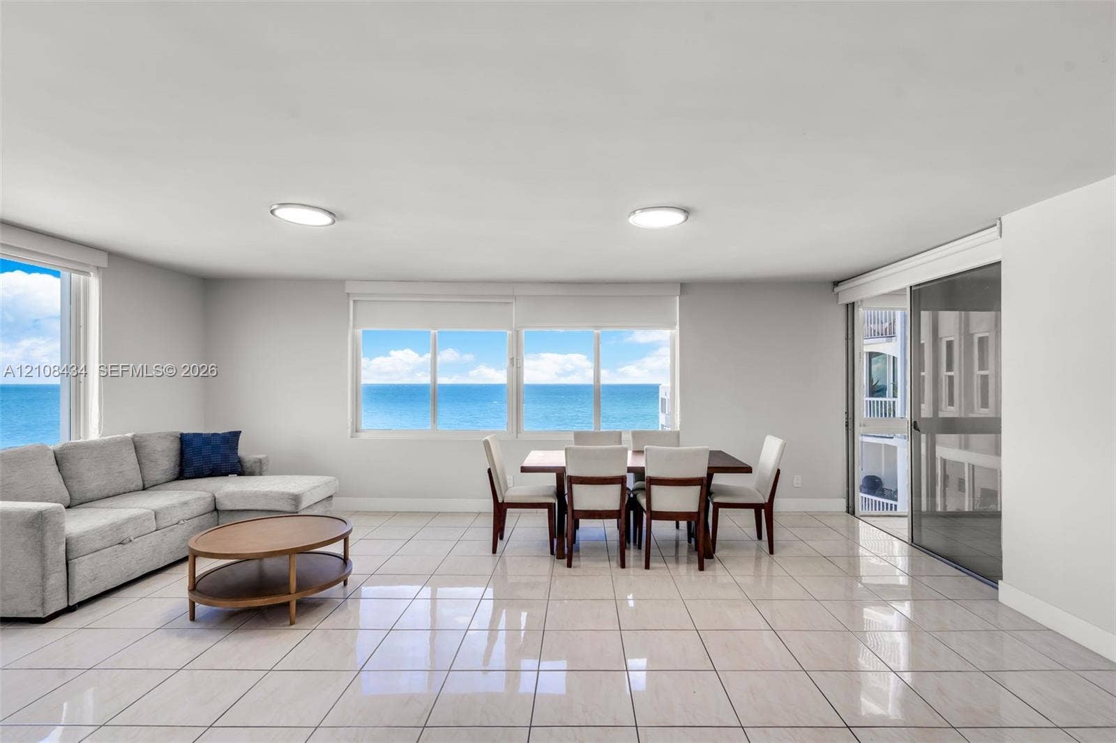Miami Beach, FL 33140 Open-concept room featuring light-toned tile flooring, large multi-pane windows, and a sliding glass door providing access to a balcony with an ocean backdrop