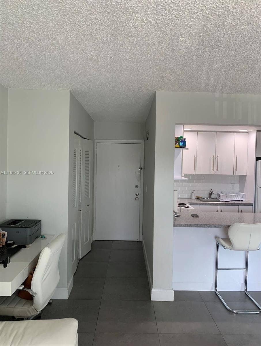 4275 S Tamiami Canal Drive, #2-314, Miami, Miami, FL 33126 Entryway with large-format tile flooring, louvered-door closet, and kitchen featuring white cabinetry, subway tile backsplash, and stone-surface breakfast bar