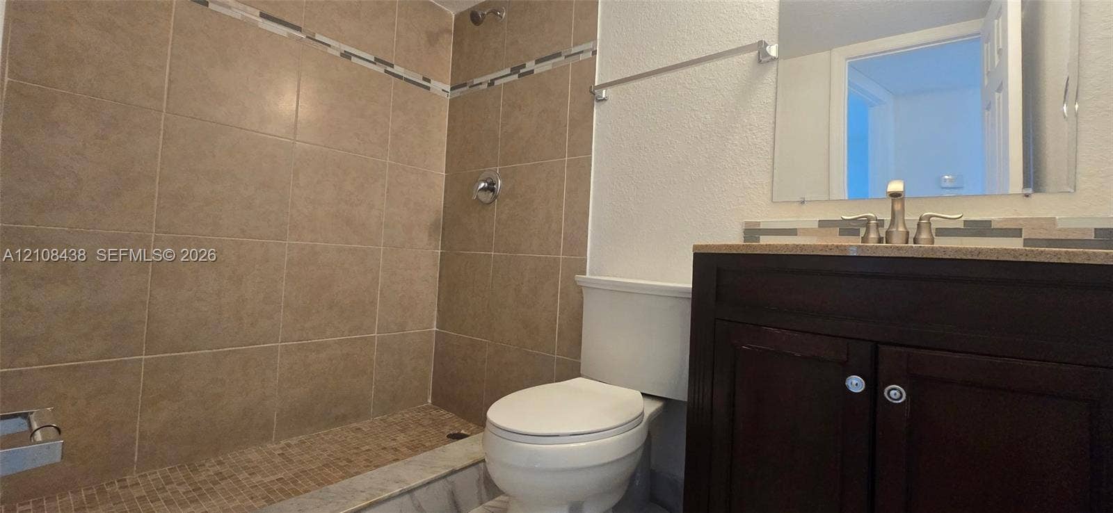 7320 NW 85th Court, #102, Tamarac, FL 33321 Bathroom featuring a vanity with a countertop, tiled walk-in shower with decorative inlay, wall-mounted mirror, and metallic finish hardware