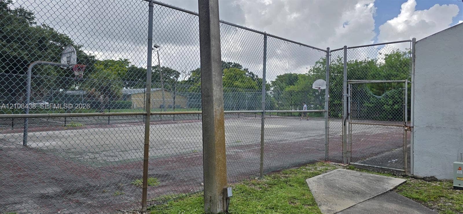 7320 NW 85th Court, #102, Tamarac, FL 33321 Recreational court featuring a hard surface, perimeter chain-link fencing, dual basketball hoops, and a gated entrance