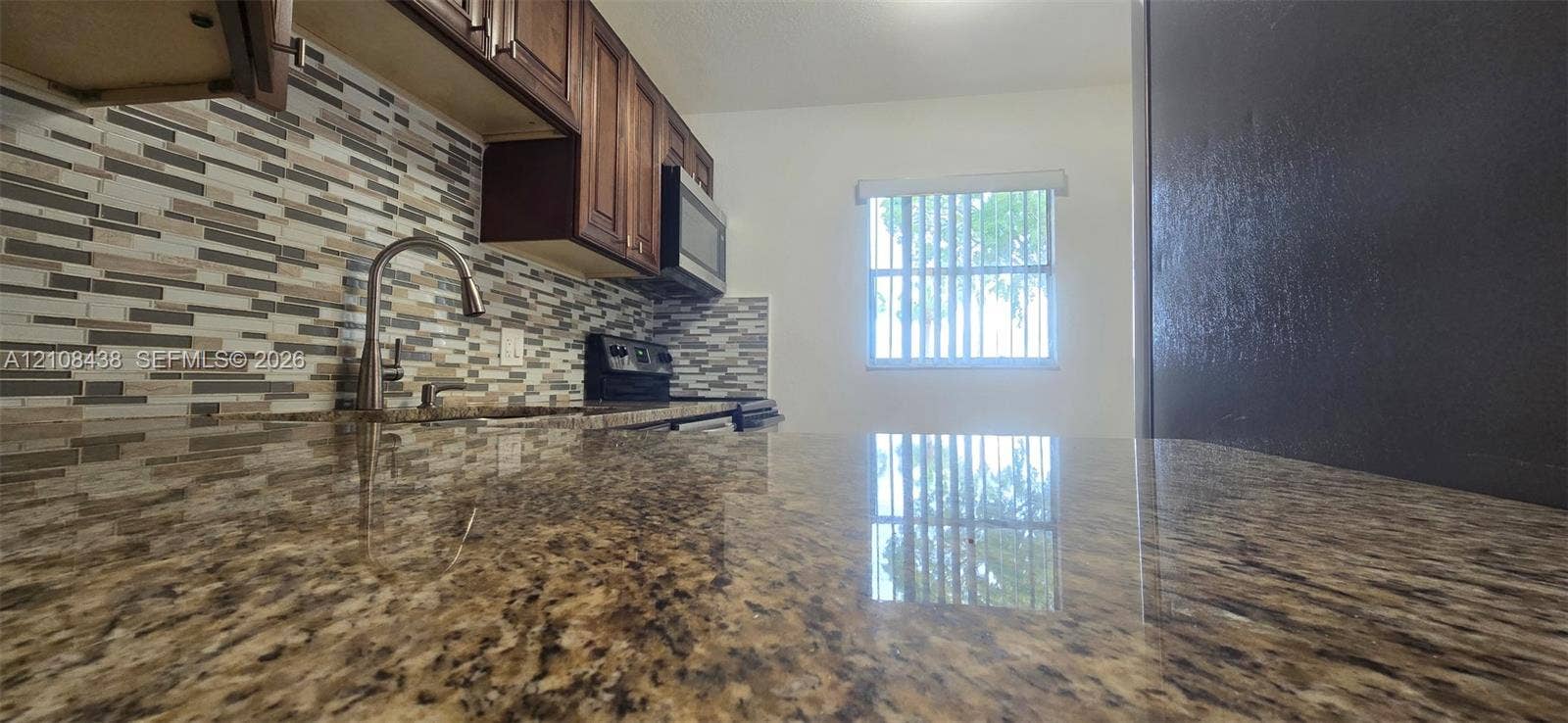7320 NW 85th Court, #102, Tamarac, FL 33321 Kitchen featuring stone-finish countertops, multi-toned linear tile backsplash, dark wood-finish cabinetry, built-in microwave, and arched faucet
