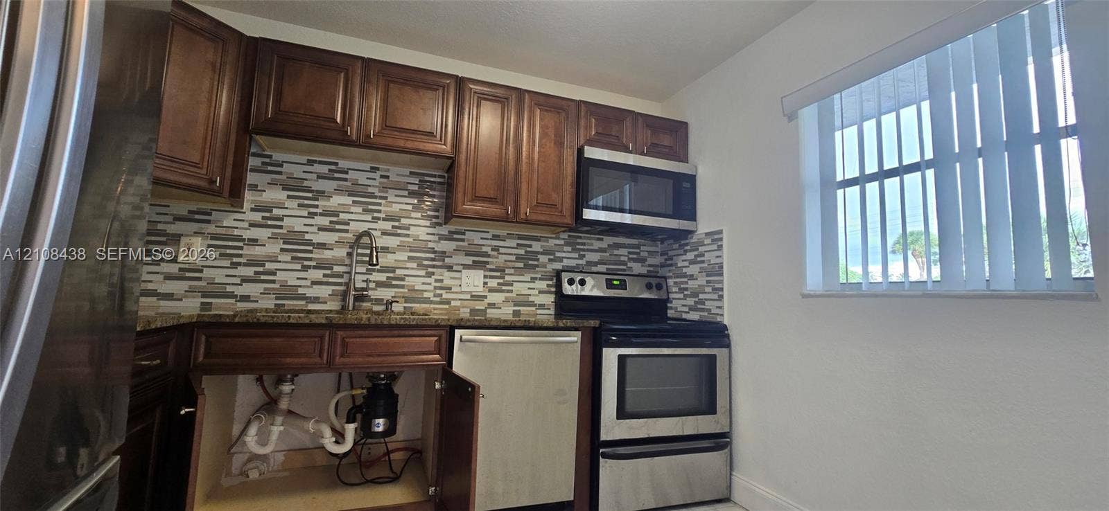 7320 NW 85th Court, #102, Tamarac, FL 33321 Kitchen featuring wood cabinetry, stone-finish countertops, decorative tile backsplash, and stainless steel appliances