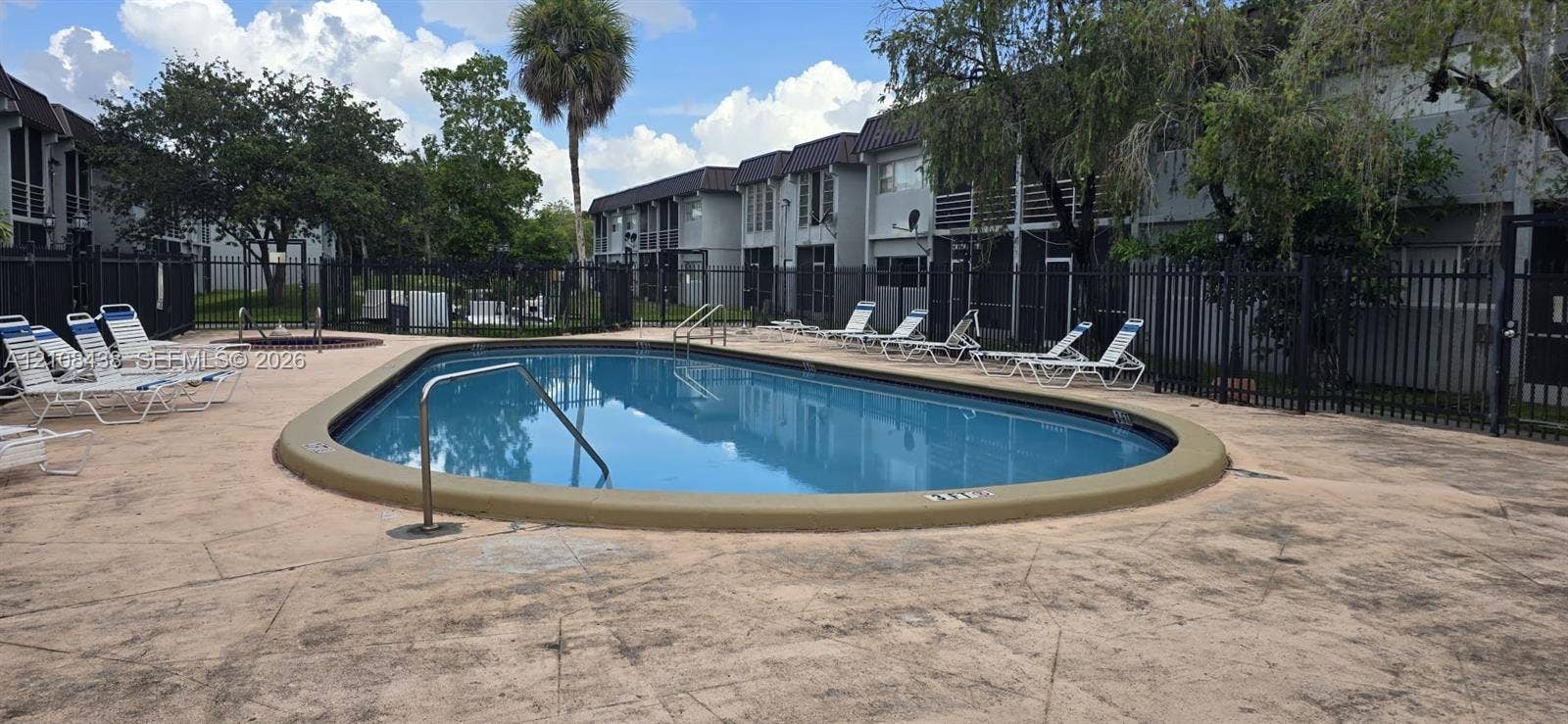 7320 NW 85th Court, #102, Tamarac, FL 33321 Oval swimming pool with metal handrails and paved pool deck, enclosed by perimeter fencing