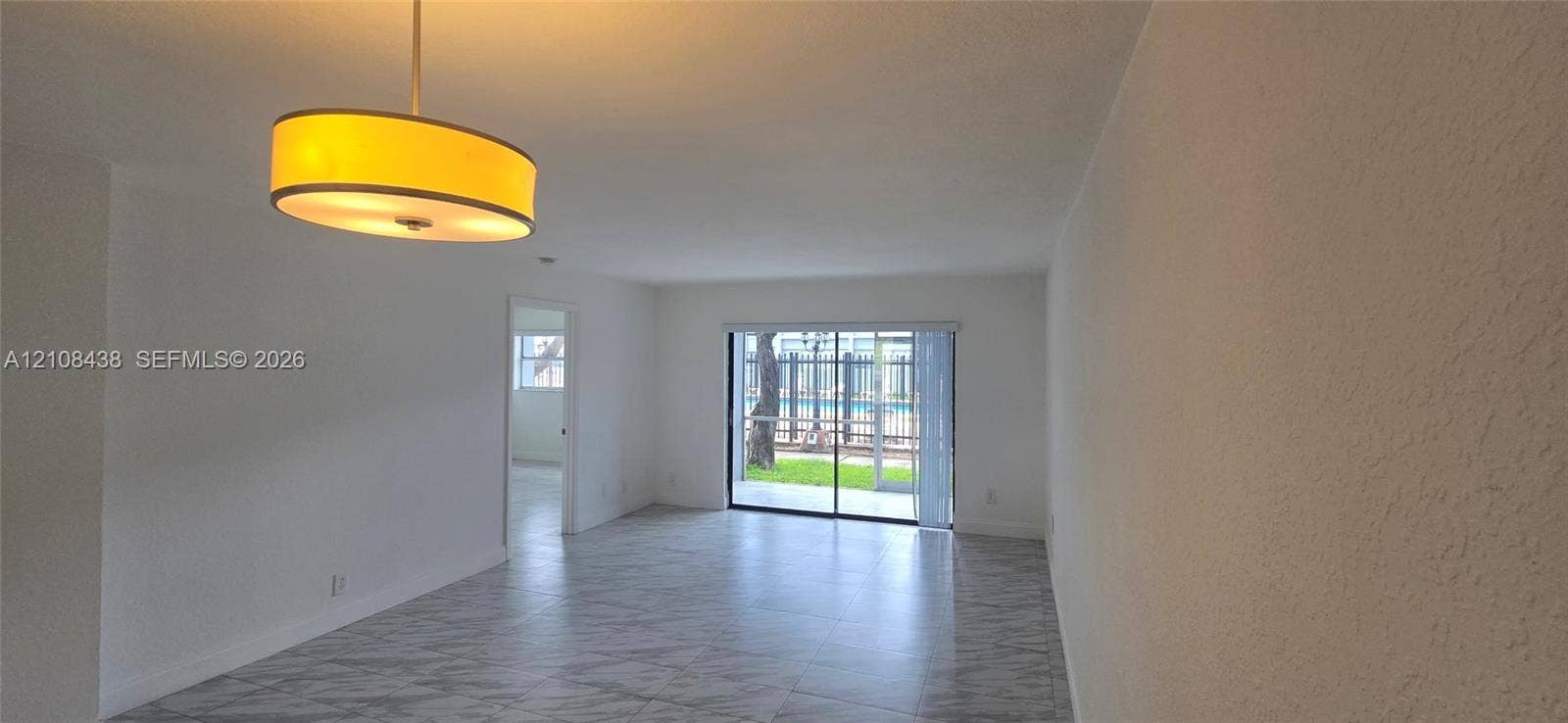 7320 NW 85th Court, #102, Tamarac, FL 33321 Neutral-toned tile flooring, suspended drum pendant light fixture, and sliding glass doors with exterior access