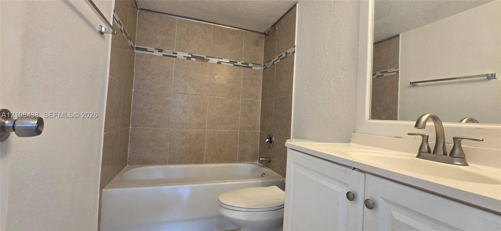 7320 NW 85th Court, #102, Tamarac, FL 33321 Bathroom featuring a white vanity cabinet with an integrated sink, satin-finish metal faucet, tub-shower combination with ceramic wall tiling, and decorative mosaic tile accent border