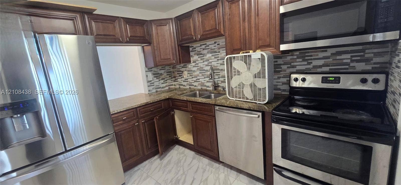 7320 NW 85th Court, #102, Tamarac, FL 33321 Kitchen featuring stained wood cabinetry, stone-finish countertops, stainless steel appliances, and a decorative tile backsplash
