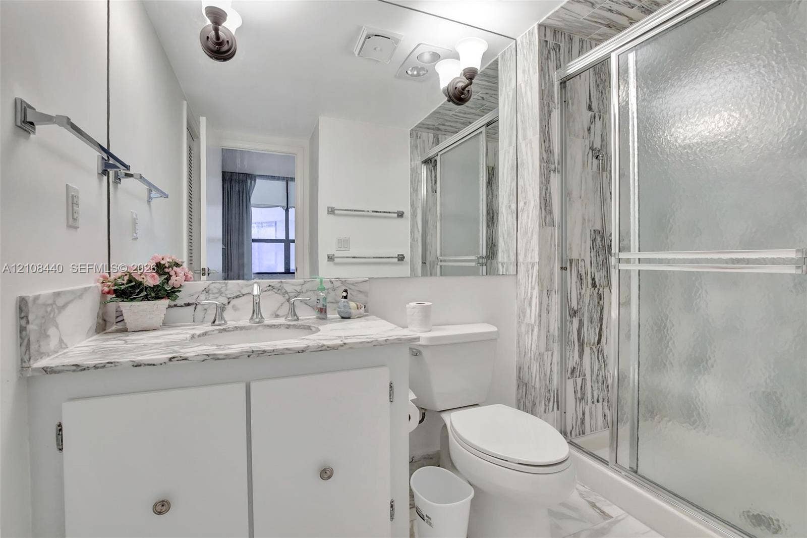 9801 Collins Avenue, #3T, Bal Harbour, Bal Harbour, FL 33154 Bathroom featuring a stone-surface vanity with an integrated sink, floor-to-ceiling stone-tiled shower enclosure, chrome-finish sliding glass shower doors, wall-to-wall mirror, and wall-mounted light fixtures