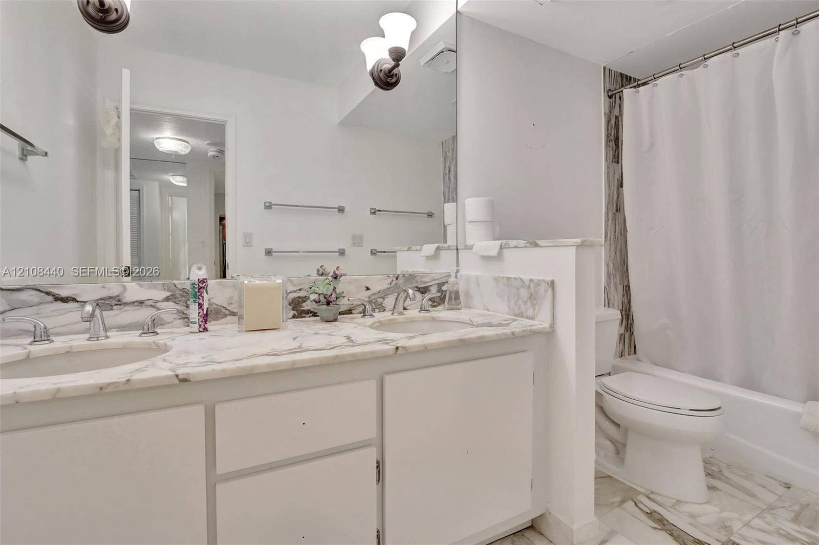 9801 Collins Avenue, #3T, Bal Harbour, Bal Harbour, FL 33154 Dual-sink vanity with stone-finish countertop and backsplash, wall-to-wall mirror, brushed metal hardware, and tub-shower combination with floor-to-ceiling stone-finish surround