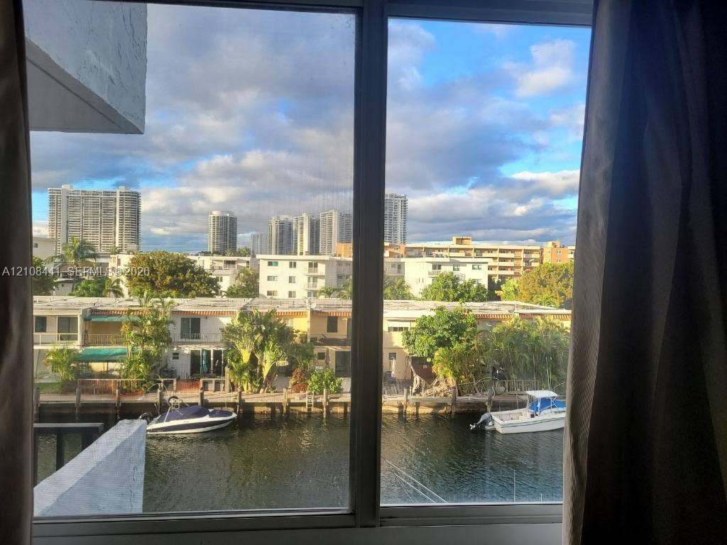 3703 NE 166th Street, #401, North Miami Beach, North Miami Beach, FL 33160 Large, multi-panel window framing a canal-side exterior featuring a private boat dock, deep-water waterway, and cityscape backdrop