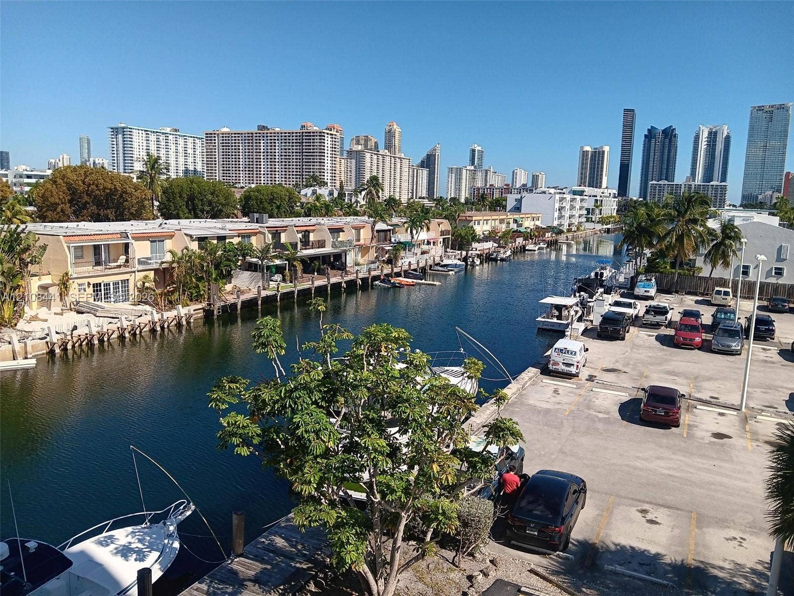 3703 NE 166th Street, #401, North Miami Beach, North Miami Beach, FL 33160 Waterfront setting featuring a concrete bulkhead, private boat slips, paved parking area, and mature palm trees