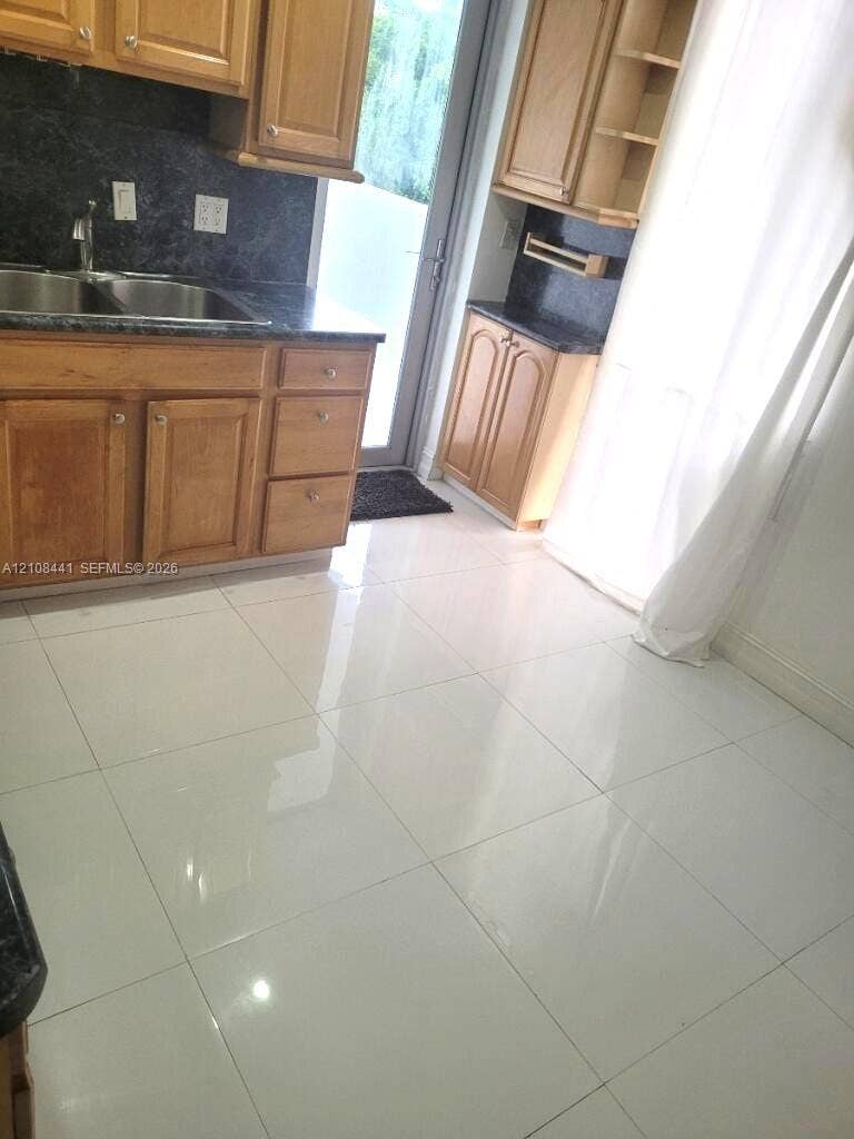 3703 NE 166th Street, #401, North Miami Beach, North Miami Beach, FL 33160 Kitchen featuring wood cabinetry, dark stone-finish countertops, dual-basin stainless steel sink, and polished white tile flooring