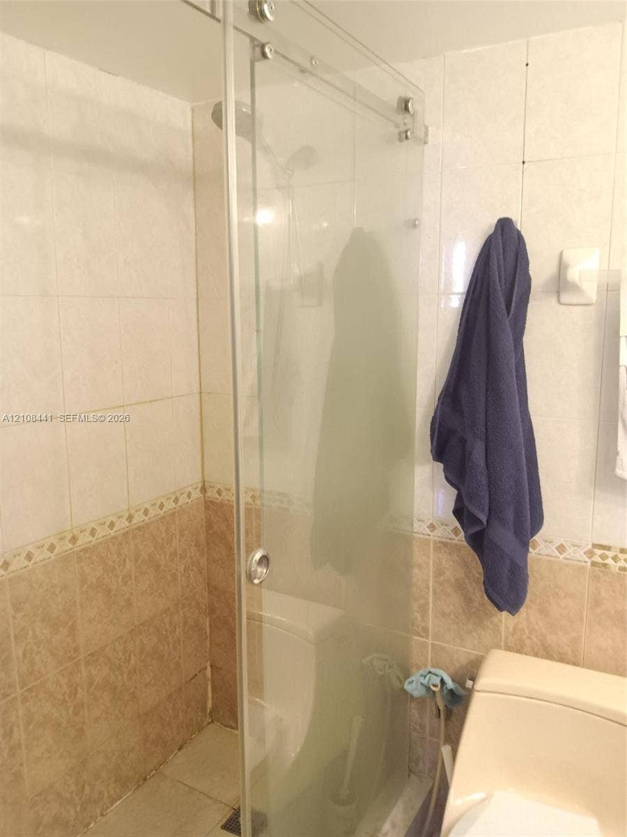 3703 NE 166th Street, #401, North Miami Beach, North Miami Beach, FL 33160 Walk-in shower featuring a frameless glass sliding door, wall-mounted shower head, and dual-tone ceramic tile surround