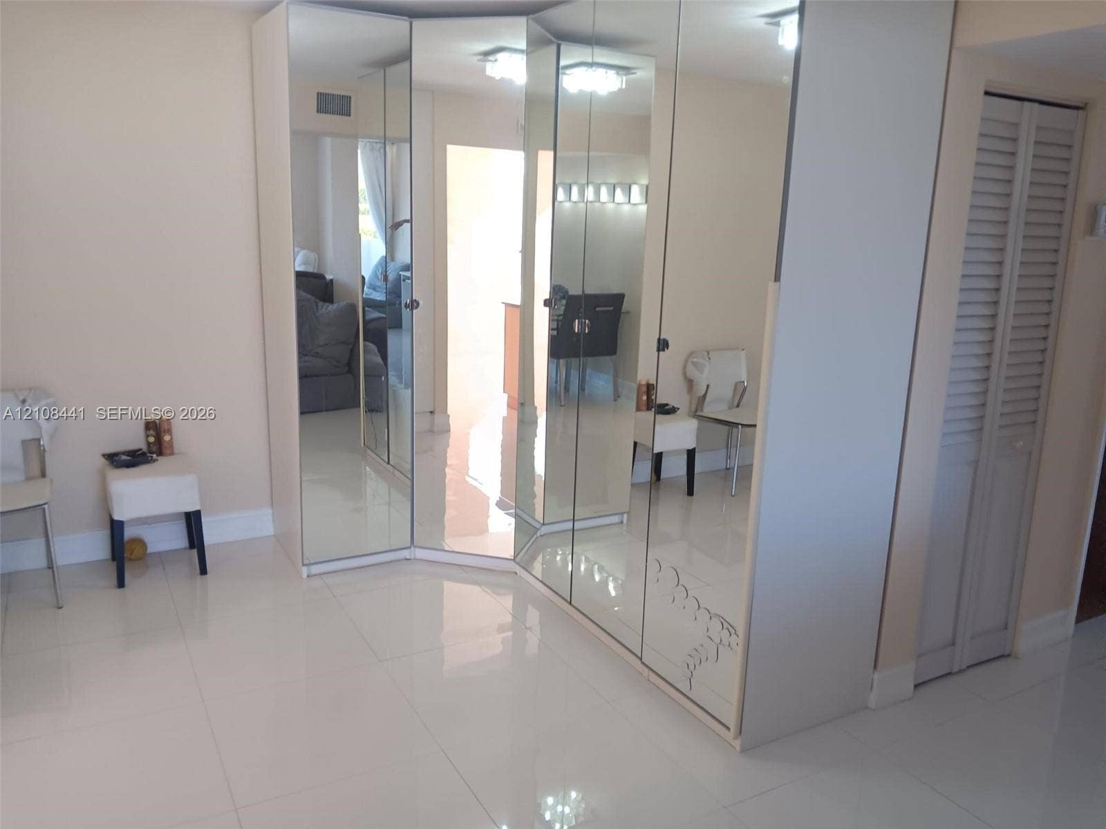 3703 NE 166th Street, #401, North Miami Beach, North Miami Beach, FL 33160 Floor-to-ceiling mirrored wardrobe featuring integrated cabinetry, reflective finish, and white tile flooring throughout, accented by louvered-panel closet doors and recessed lighting
