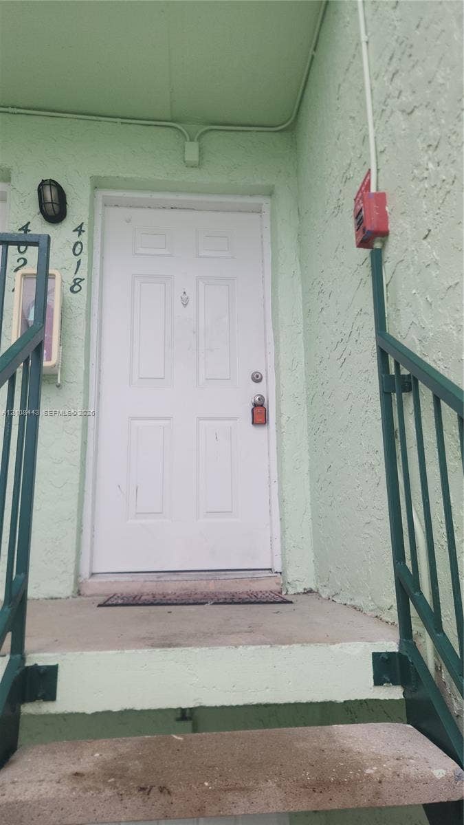 4018 NW 87th Avenue, #4018, Sunrise, Sunrise, FL 33351 Exterior entry featuring a white six-panel door, textured stucco siding, concrete stairs, and metal railings