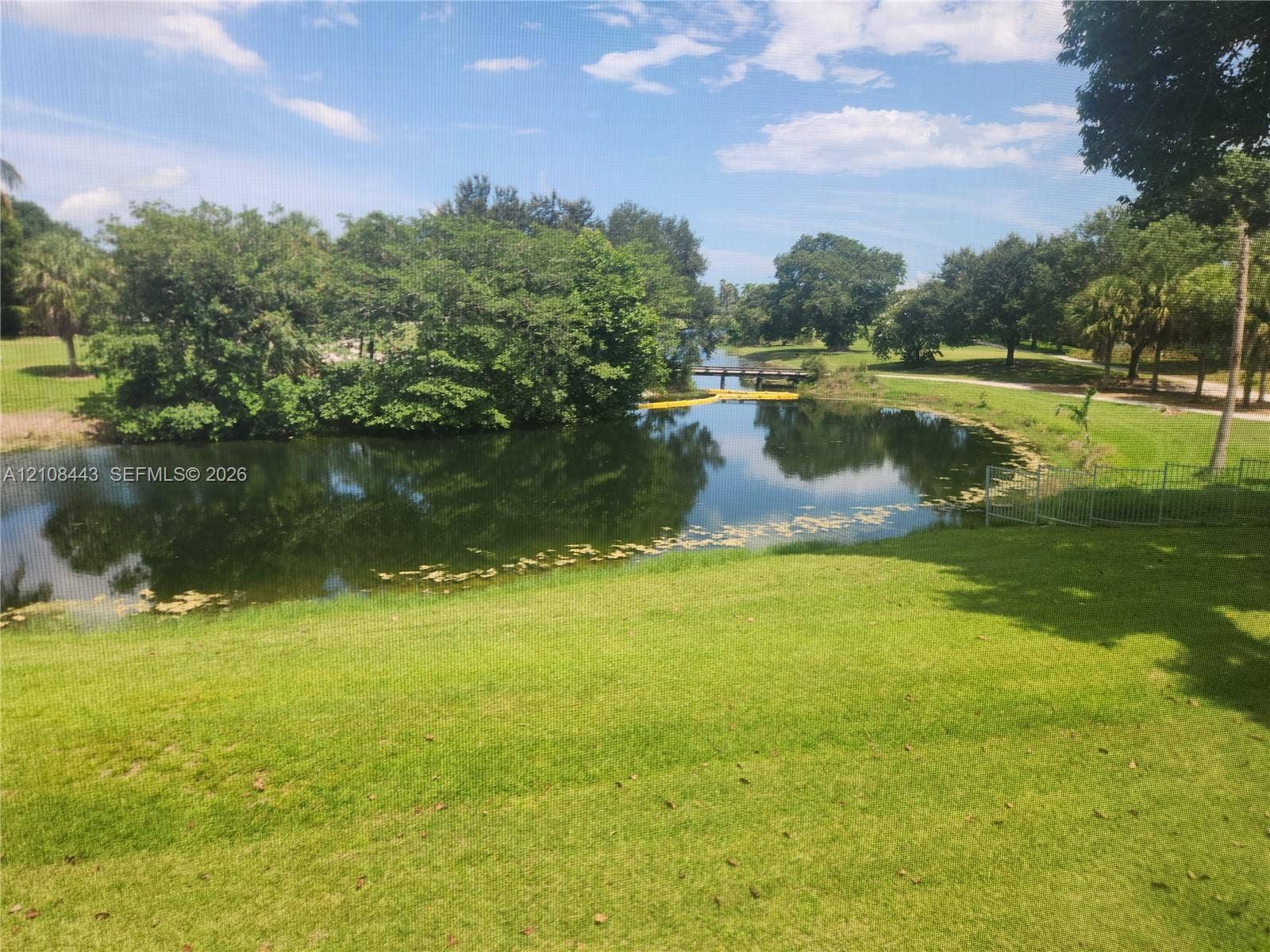 4018 NW 87th Avenue, #4018, Sunrise, Sunrise, FL 33351 Waterfront pond featuring a grass lawn, mature trees, and metal perimeter fencing
