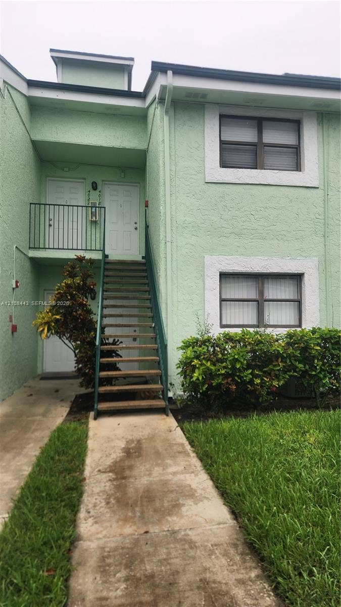 4018 NW 87th Avenue, #4018, Sunrise, Sunrise, FL 33351 Two-story exterior featuring a textured stucco finish, white window trim, a metal staircase with railings, and a concrete walkway