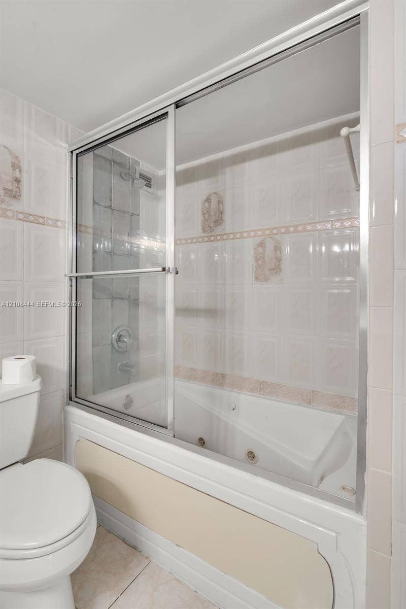 Jetted soaking tub with integrated shower, sliding glass enclosure, and wall-mounted plumbing fixtures surrounded by ceramic tile wall accents
