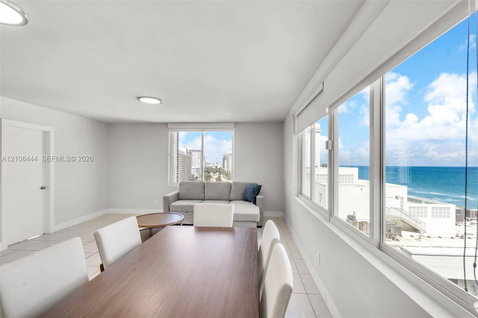 Open interior space with large-format tile flooring, flush-mount lighting, and extensive windows showcasing ocean and coastline scenery