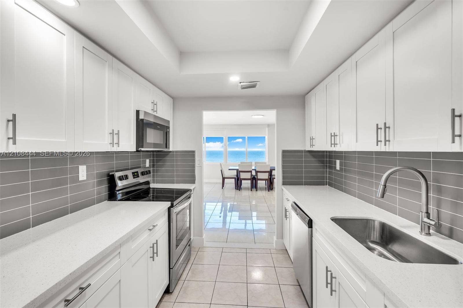 Kitchen featuring white shaker-style cabinetry, solid-surface countertops, horizontal gray tile backsplash, stainless steel appliances, and large-format tile flooring