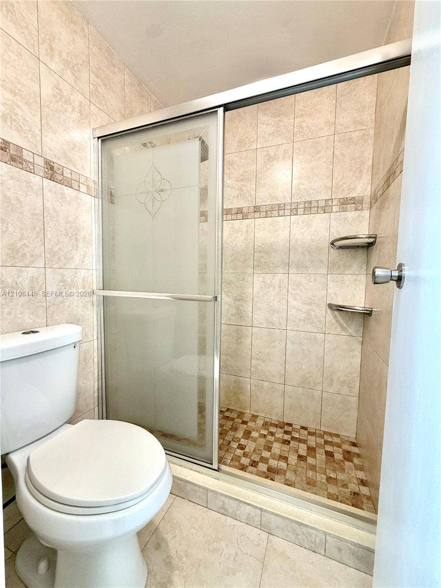 800 W 81st Place, Hialeah, Hialeah, FL 33014 Shower enclosure featuring a sliding glass door with frosted detailing, neutral-toned tiled wall surrounds with decorative mosaic accents, integrated shower shelving, and a patterned tiled shower floor