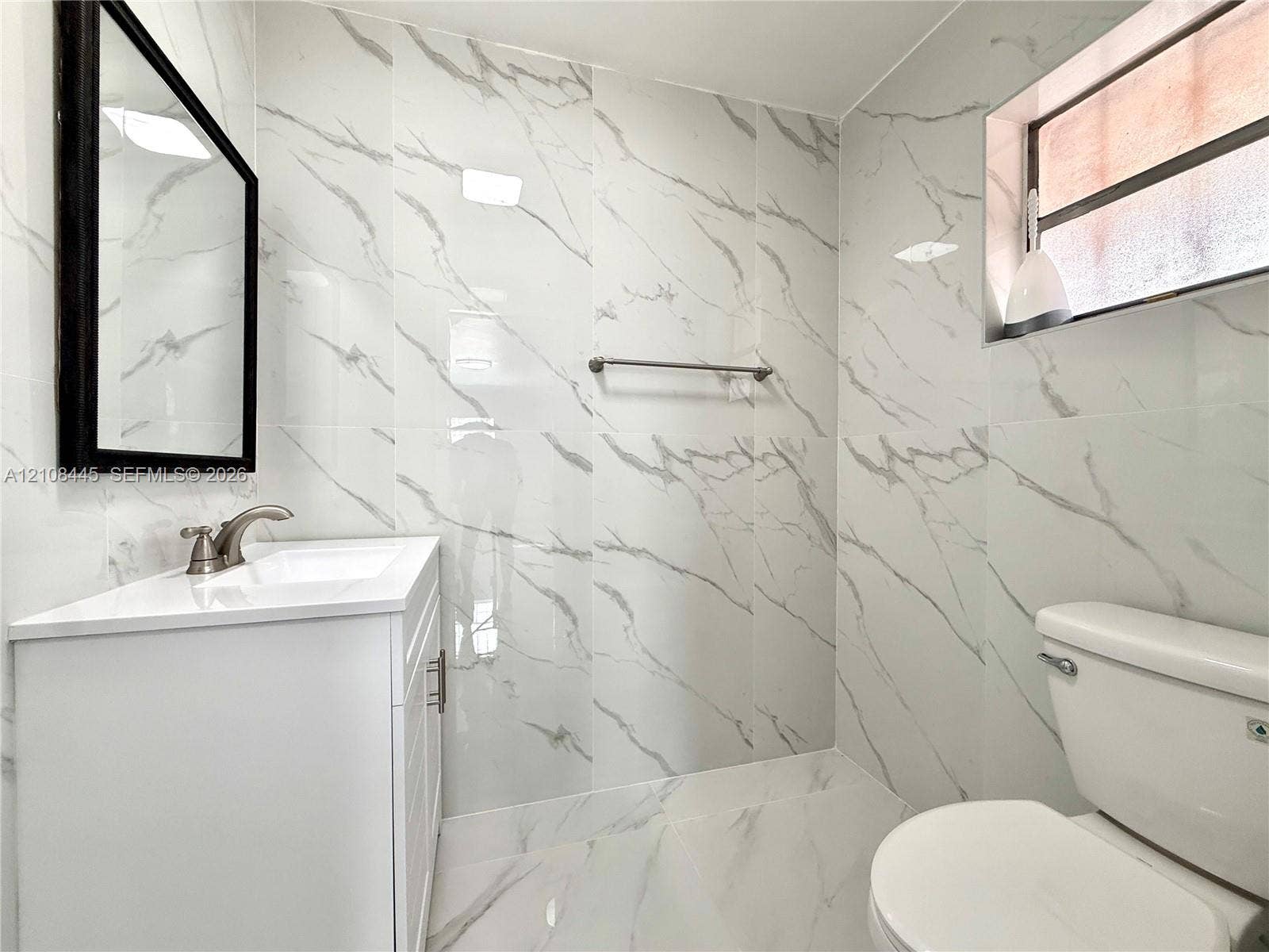 800 W 81st Place, Hialeah, Hialeah, FL 33014 Guest Bathroom featuring white veined wall and floor tile, white vanity cabinet with integrated sink, rectangular black-framed wall mirror, and brushed-finish metal faucet and hardware
