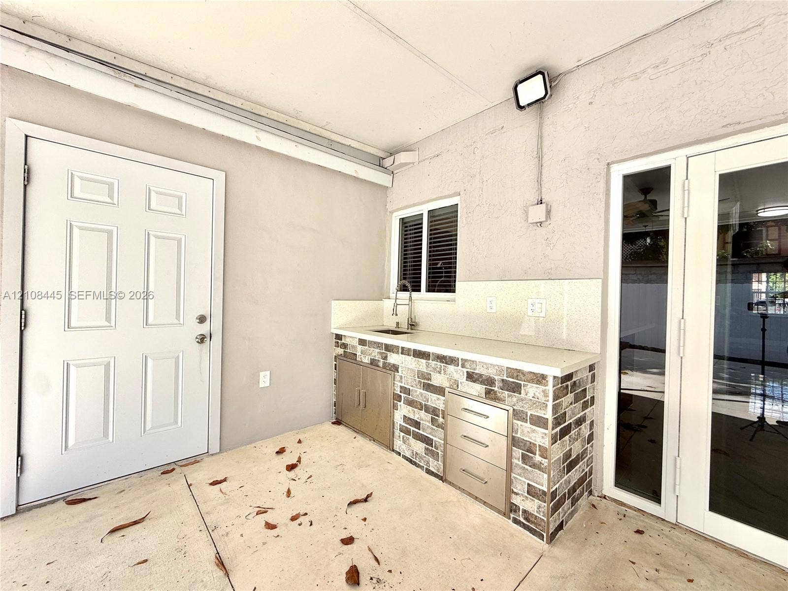 800 W 81st Place, Hialeah, Hialeah, FL 33014 Covered outdoor kitchen area featuring a stone-veneer base, solid surface countertop, stainless steel integrated sink, and built-in metal cabinetry