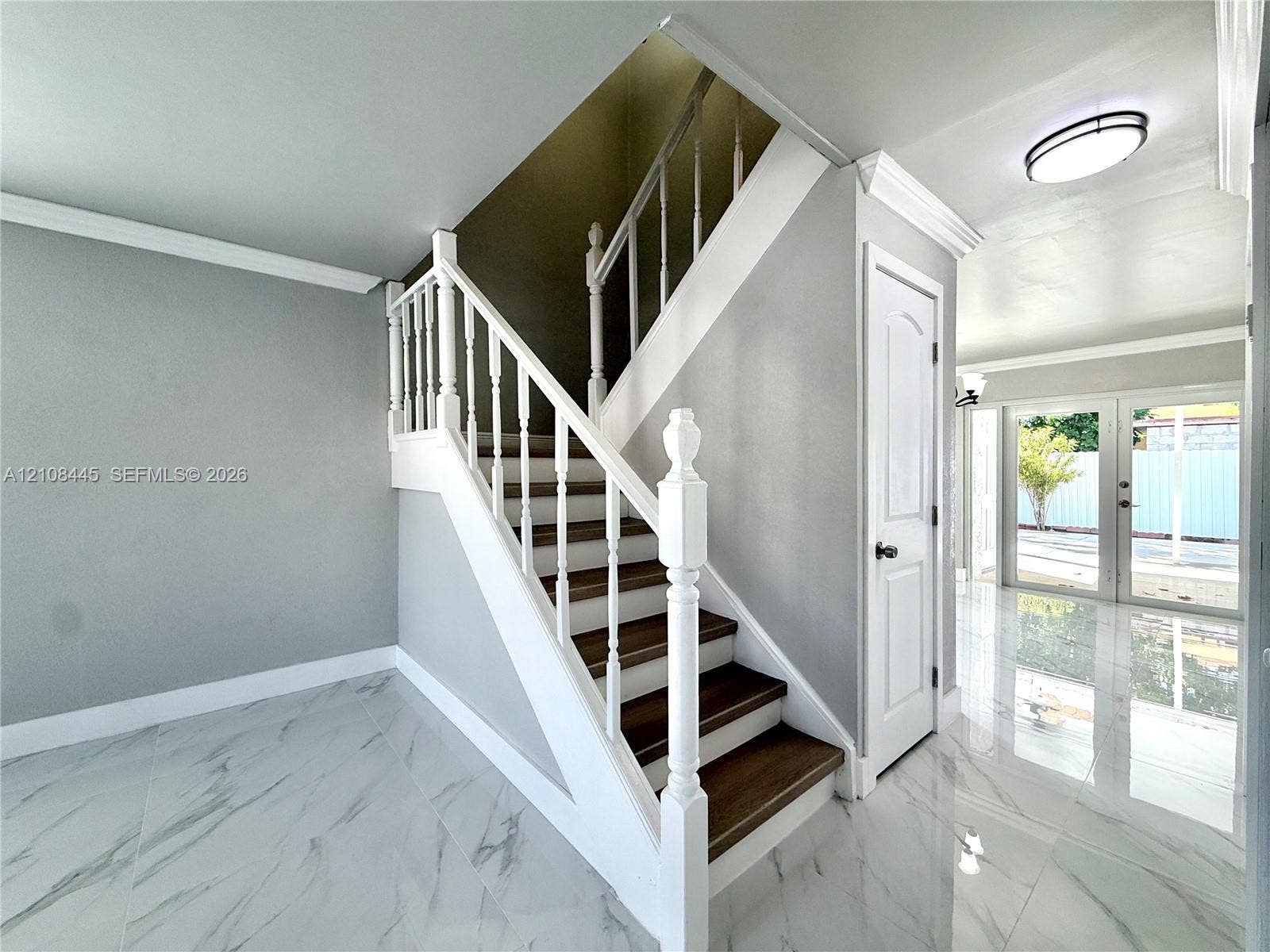 800 W 81st Place, Hialeah, Hialeah, FL 33014 Staircase featuring dark wood-finish treads, white balusters, and a decorative newel post, complemented by polished stone-finish flooring and double-panel glass doors