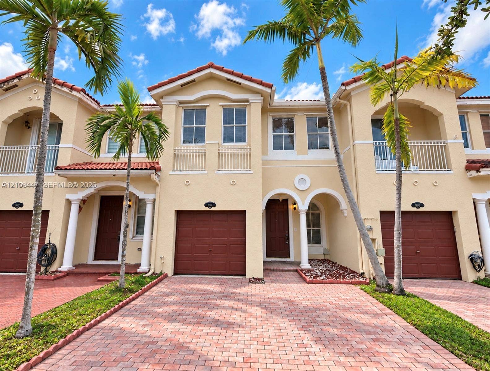 Stucco exterior featuring arched entryways, tile roofing, second-story balconies, and paver driveways