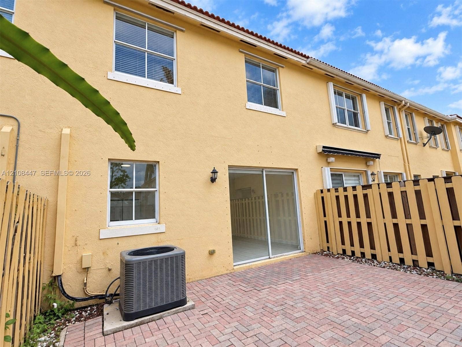 Stucco exterior featuring a brick paver patio, sliding glass door, and wooden privacy fencing