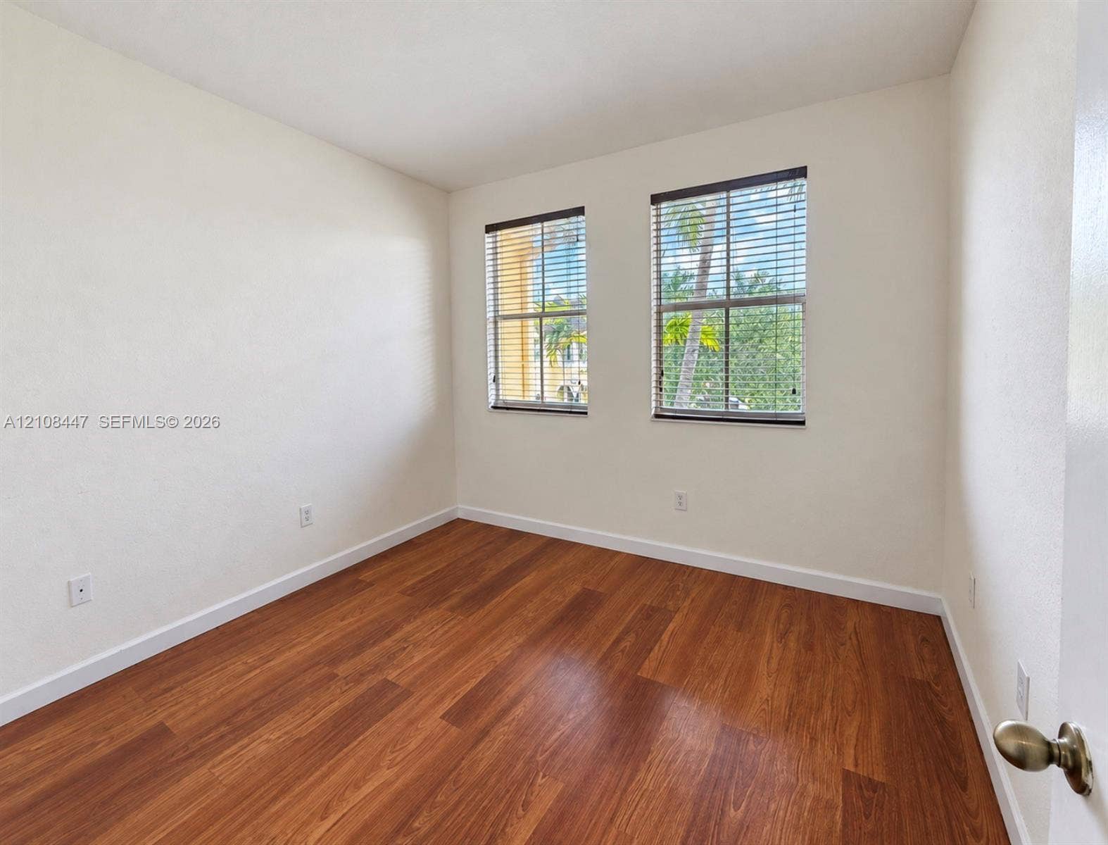 Interior room featuring wood-finish flooring, neutral walls, and two windows with horizontal blinds
