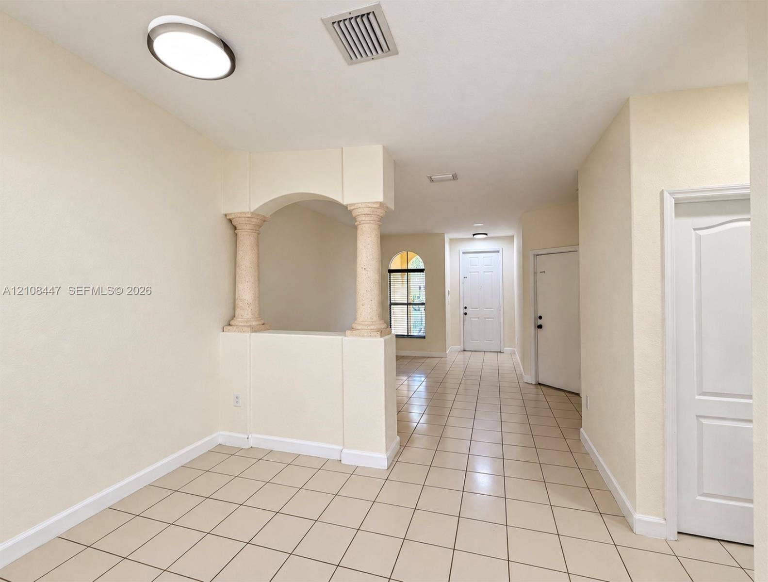 Interior space featuring decorative stone-texture columns, an arched architectural opening, ceramic tile flooring, and a multi-panel door with an arched window