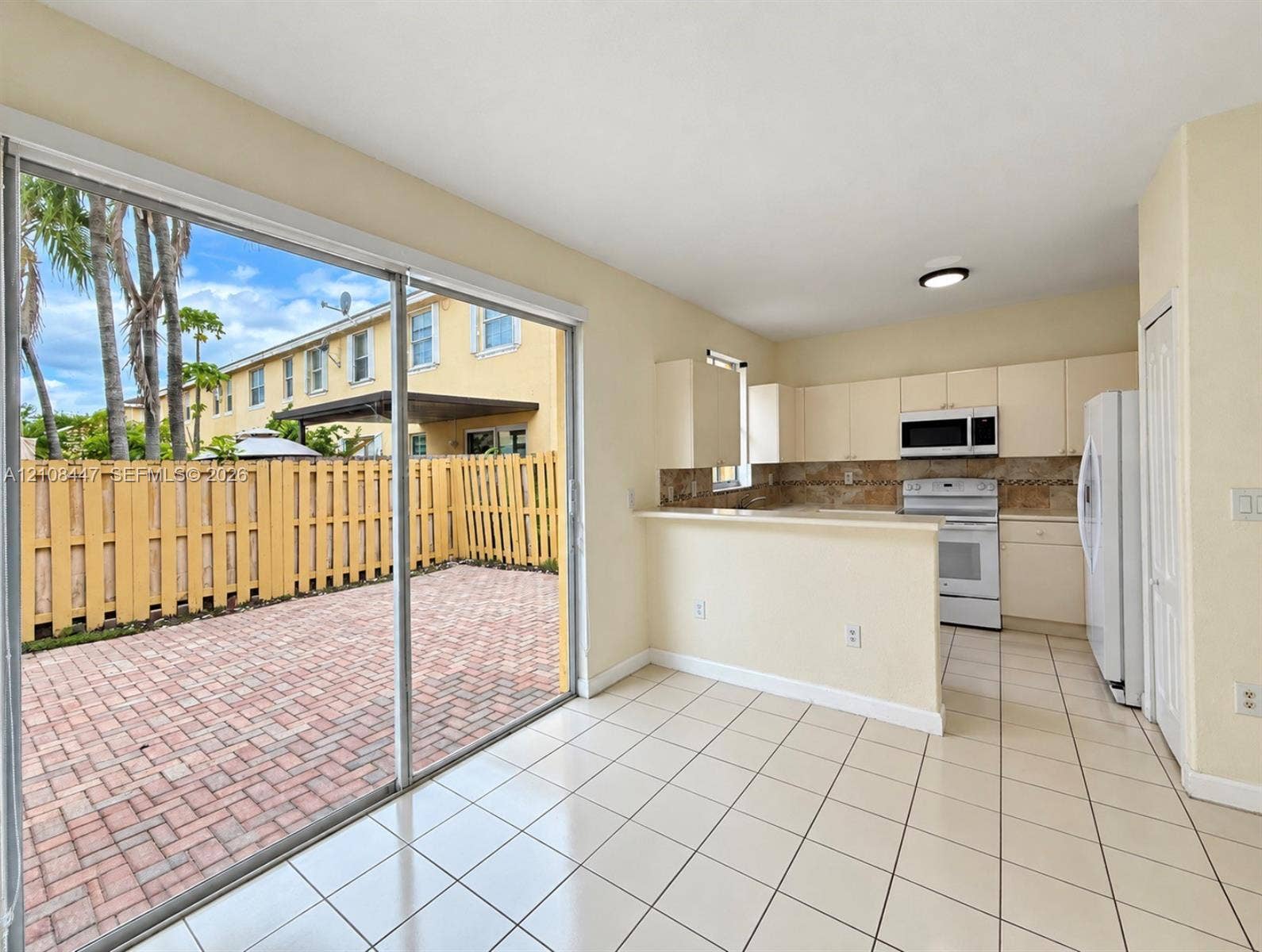 Kitchen featuring white cabinetry, an integrated microwave, and a breakfast bar, with ceramic tile flooring and sliding glass doors opening to a brick-paver patio